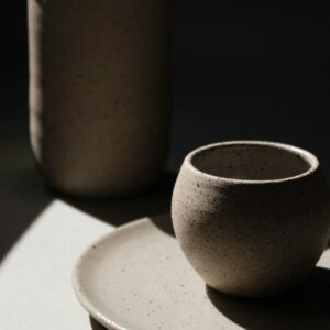 A charcoal stoneware cup on a matching saucer beside a tall jug