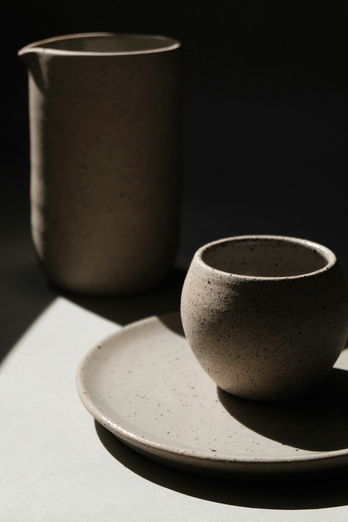 A charcoal stoneware cup on a matching saucer beside a tall jug