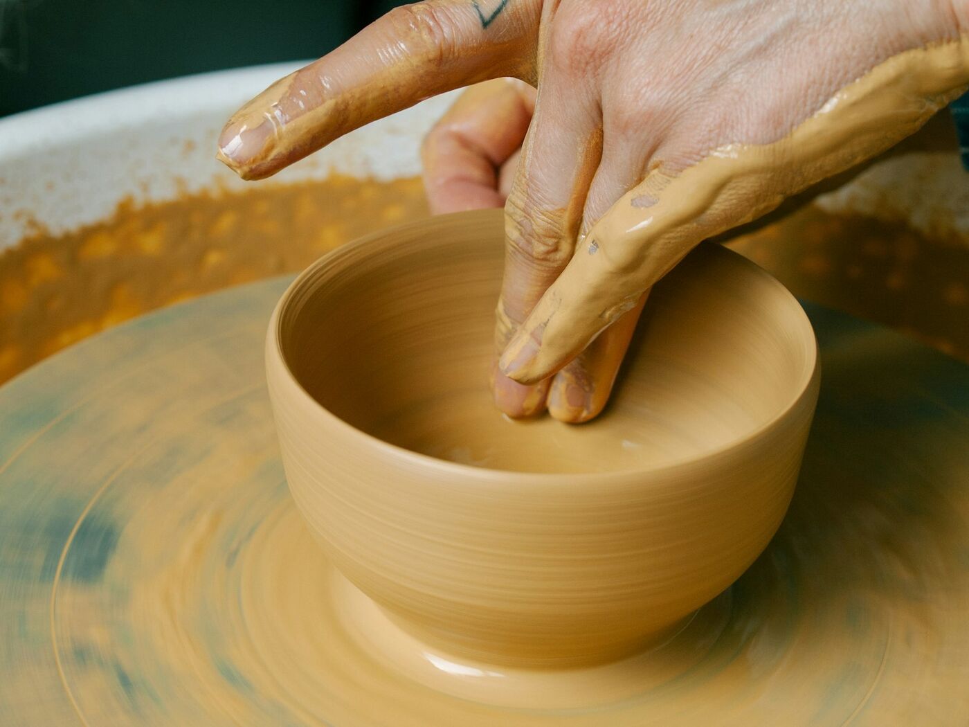 Clay-covered hands shaping a bowl on a spinning wheel in warm light