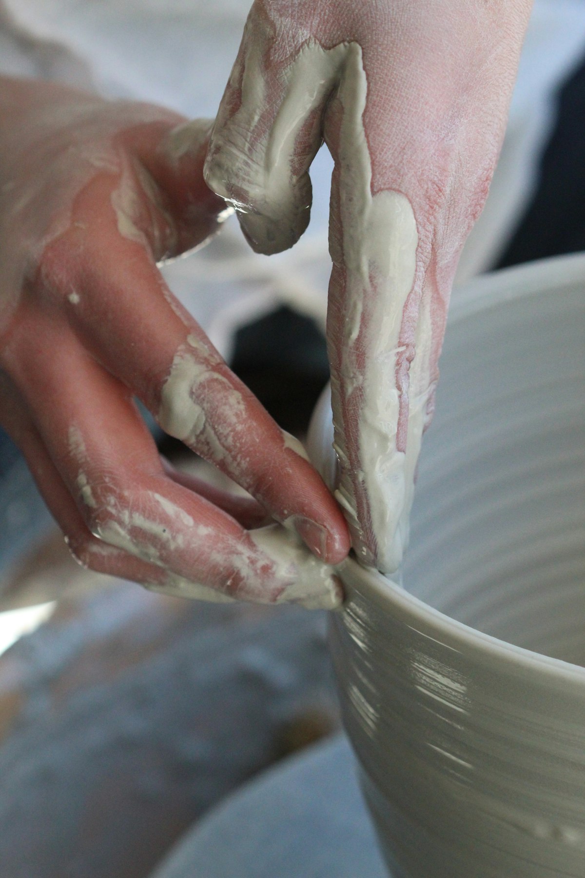 Clay-covered hands smoothing the rim of a bowl
